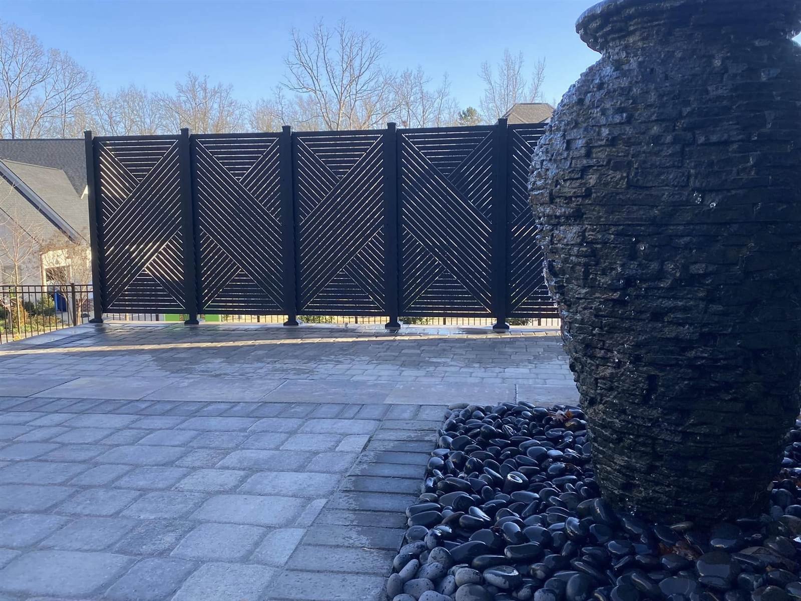 Modern black louvered privacy screen atop a stone retaining wall